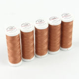 Fünf Spulen kupferfarbenes Ackermann Universal Nähgarn Stärke 120 (Farbe 0763 kupfer) mit weißen Etiketten sind nebeneinander auf einem weißen Hintergrund angeordnet. Dieses Set von ACKERMANN® enthält fünf 200-m-Spulen hochwertigen, strapazierfähigen Polyestergarn, das sich ideal für eine Vielzahl von Nähprojekten eignet.