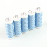 Fünf Spulen ACKERMANN® Stickgarn Stärke 40 (Farbe 2989 hellblau, 5 × 260 m) sind auf einem weißen Hintergrund in einer Reihe angeordnet. Jede Spule hat eine weiße Kappe mit rotem und schwarzem Schriftzug.