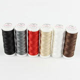 Sechs Garnspulen in den Farben Schwarz, Grau, Rot, Beige, Weiß und Braun stehen aufrecht in einer Reihe auf einer weißen Unterlage. Diese hochwertigen Spulen sind Teil des Sets „Ackermann Nähgarn Leather Mix 6x 120 m Stärke 60“ von ACKERMANN® – perfekt für allgemeine Näharbeiten und als strapazierfähiges Ledernähgarn.