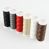 Sechs Spulen ACKERMANN® Ackermann Nähgarn „Leather Mix“ 6 × 120 m, Stärke 60, in den Farben Schwarz, Dunkelgrau, Rot, Beige, Weiß und Braun sind auf weißem Hintergrund in einer Reihe angeordnet.
